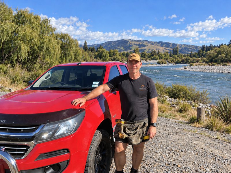 Allan McLean wearing a Special Solutions Flood Protection shirt beside his ute; digitally edited river backdrop.
